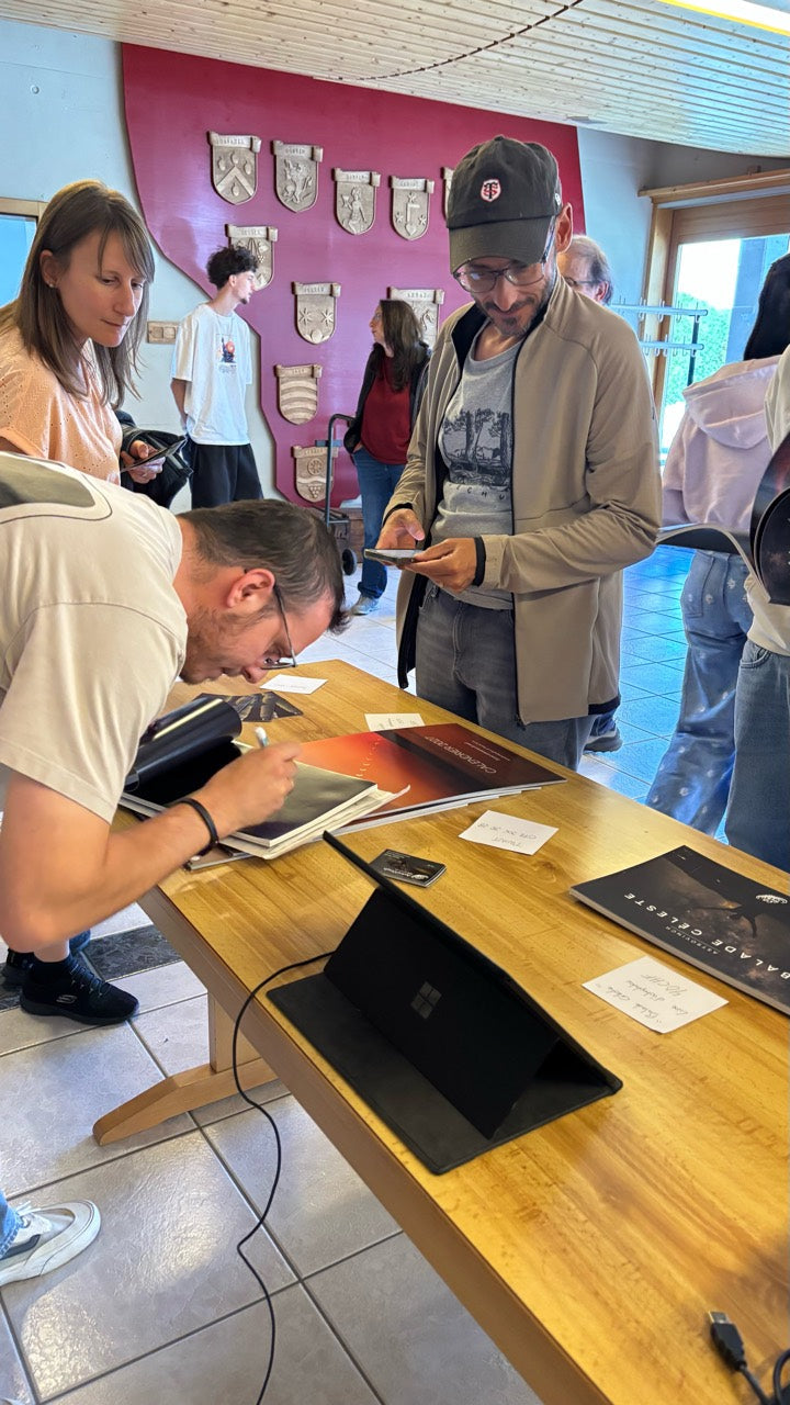 Une personne dédicace un calendrier sur une table où sont présentés des calendriers AstroVinch 2027, entourée de visiteurs.