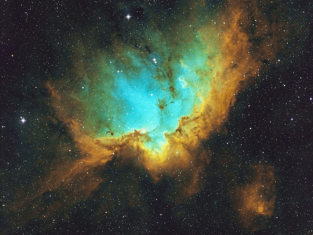 Nébuleuse du Sorcier aux teintes turquoise et dorées, découpée par des silhouettes de poussière sombre.