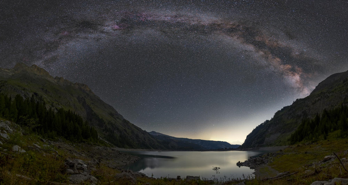 Arche étoilée de la Voie lactée au-dessus d’un lac du Rawyl, entre des montagnes et des rives rocheuses.