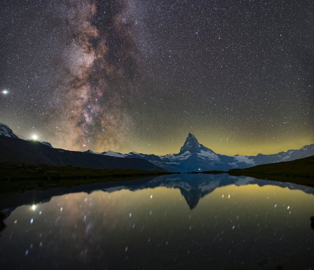 Cervin et Voie lactée verticale reflétés dans l’eau calme du Stellisee, entre des rives sombres.