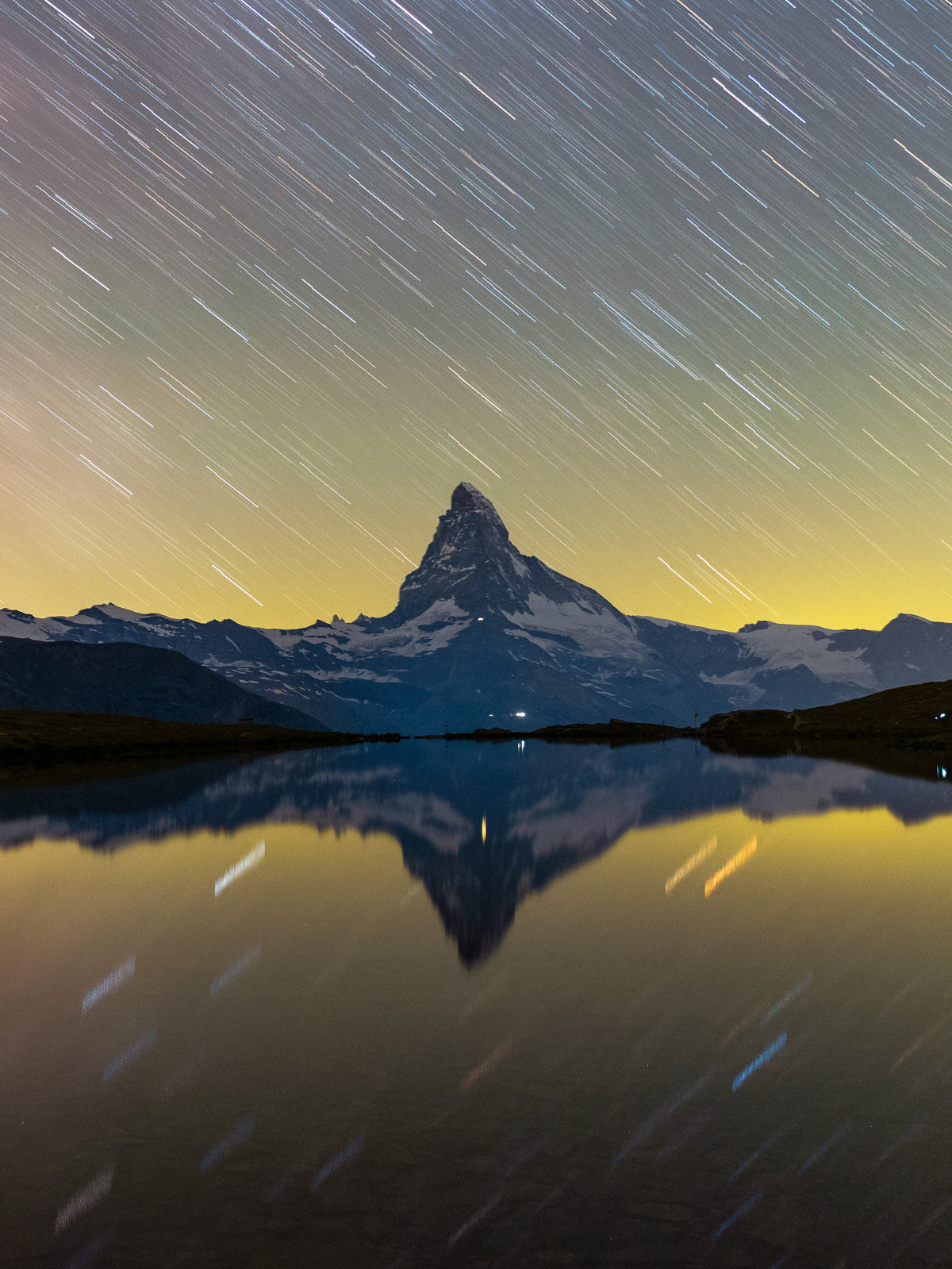 Cervin sous des traces d’étoiles courbes, reflété avec le ciel dans une eau sombre et calme.