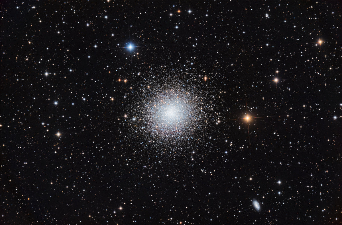 Grand amas d’Hercule au cœur blanc très dense, entouré d’étoiles blanches et orangées.