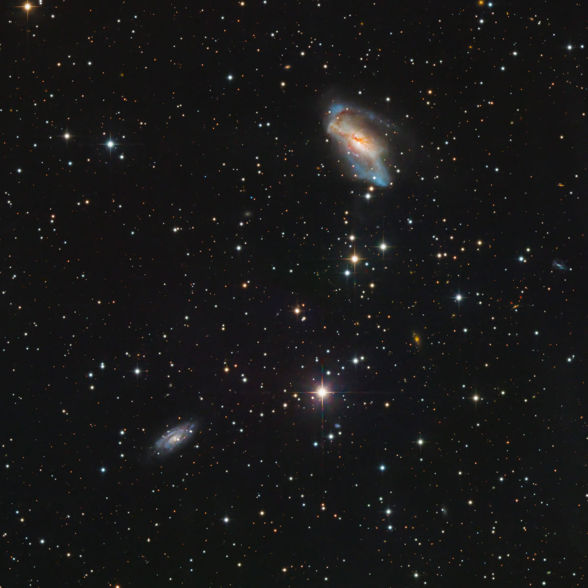 Petite galaxie lumineuse et irrégulière parmi des étoiles et plusieurs faibles silhouettes de galaxies.