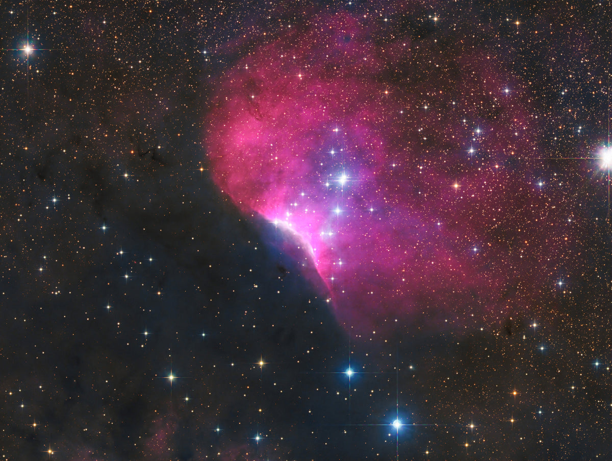 Nébuleuse rose et bleutée de Sh2-140, bordée de nuages sombres et ponctuée d’étoiles brillantes.