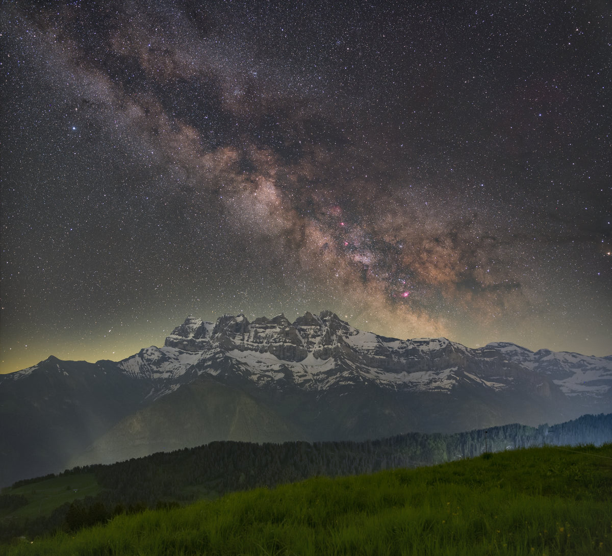 Bande lumineuse de la Voie lactée au-dessus des Dents du Midi, avec une prairie sombre au premier plan.