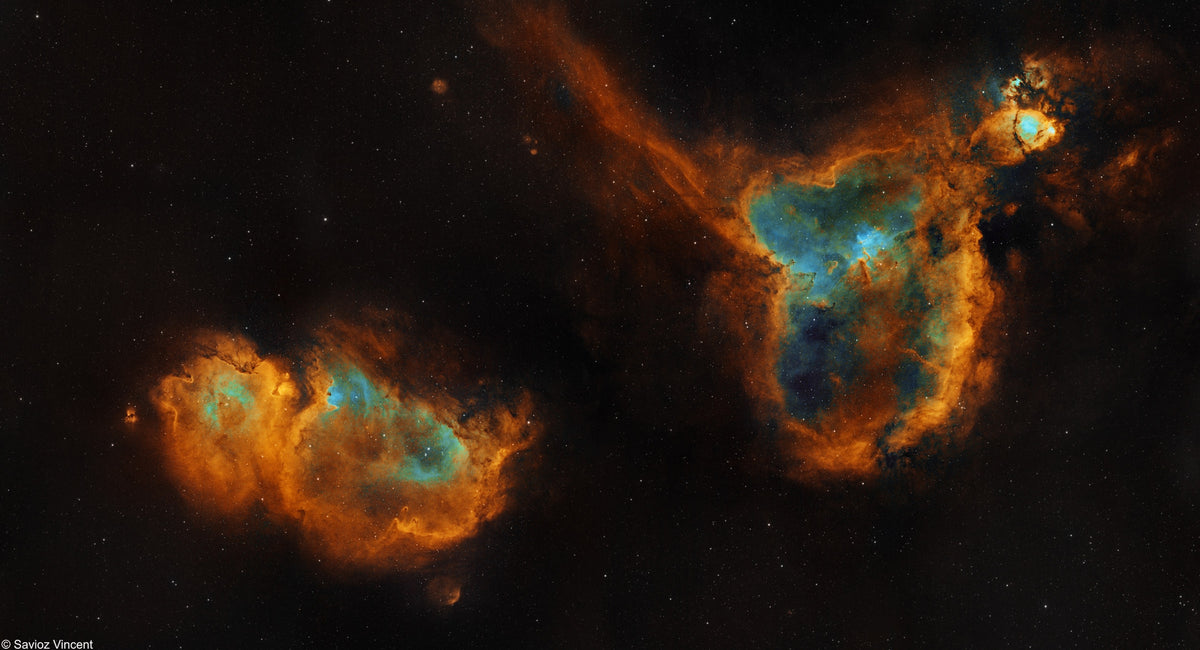 Deux grandes nébuleuses aux contours orangés et aux centres bleutés, reliées par des nuages de gaz.