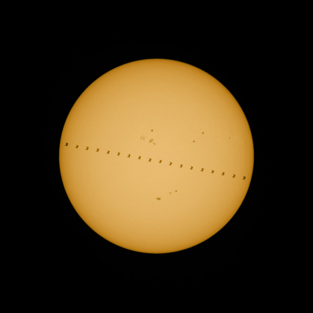 Disque solaire jaune sur fond noir, traversé par une succession de petites silhouettes sombres de l’ISS.