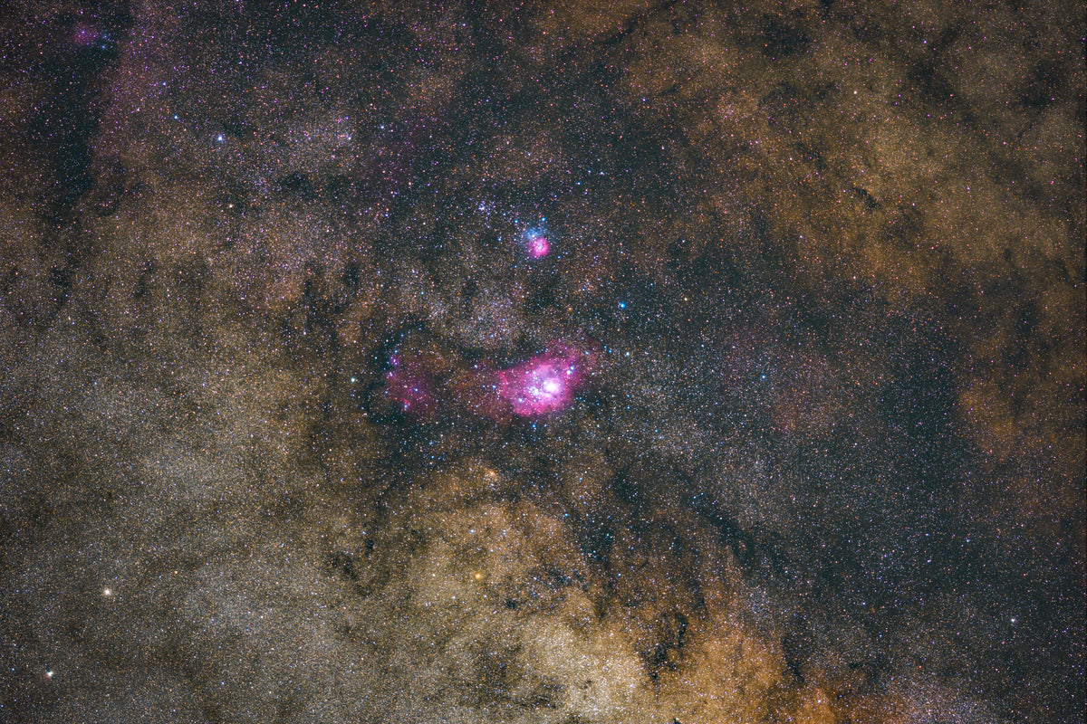 Deux nébuleuses roses et bleutées dans un vaste champ stellaire traversé par des nuages de poussière sombres.