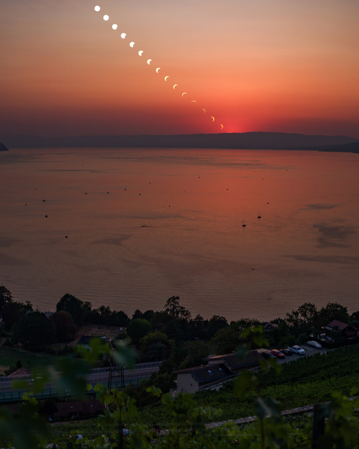 Disques successifs du Soleil en diagonale dans un ciel orange, au-dessus du lac et de silhouettes d’arbres.