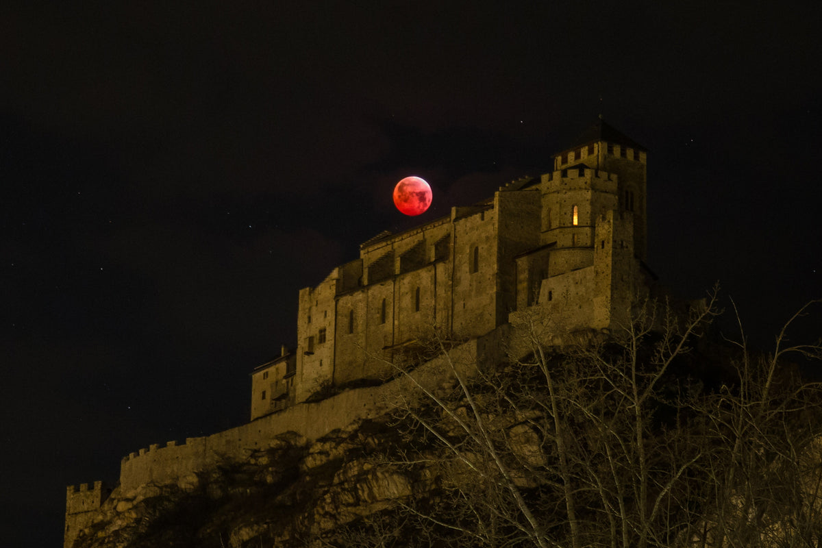 Disque rouge de la Lune au-dessus de la basilique de Valère éclairée, sur sa colline.