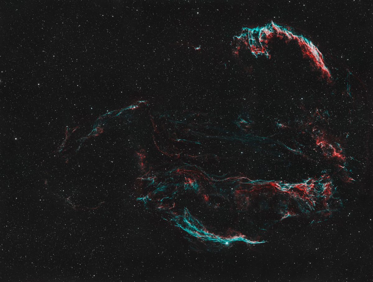 Longs filaments rouges et bleutés des Dentelles du Cygne, formant des arcs dans un champ d’étoiles.