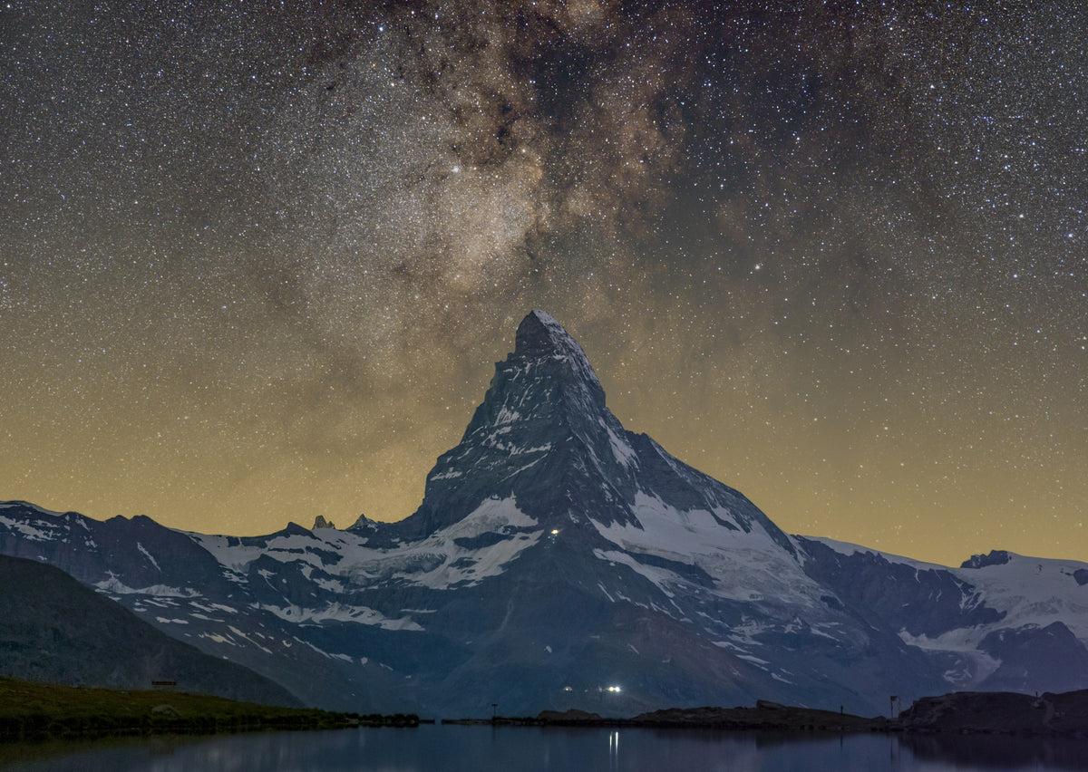 Sommet du Cervin enneigé devant une bande de la Voie lactée et un ciel dense en étoiles.