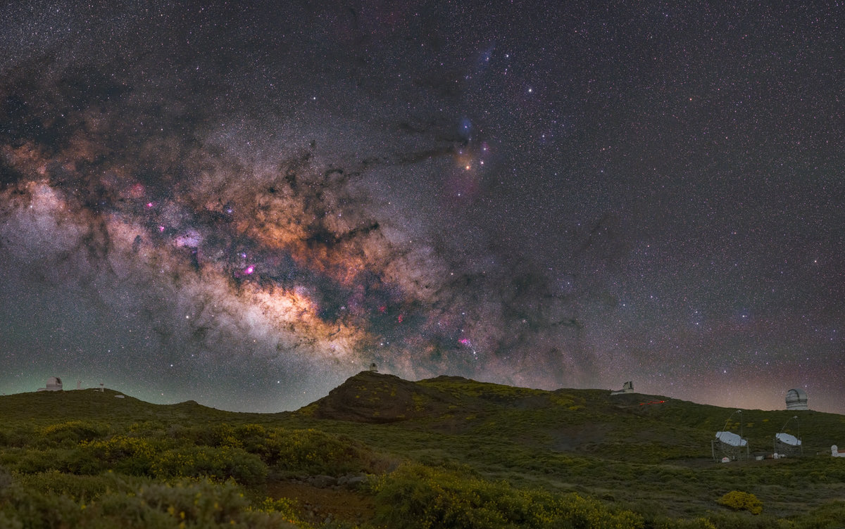 Large bande de la Voie lactée au-dessus des collines de La Palma, avec des bâtiments d’observation à l’horizon.