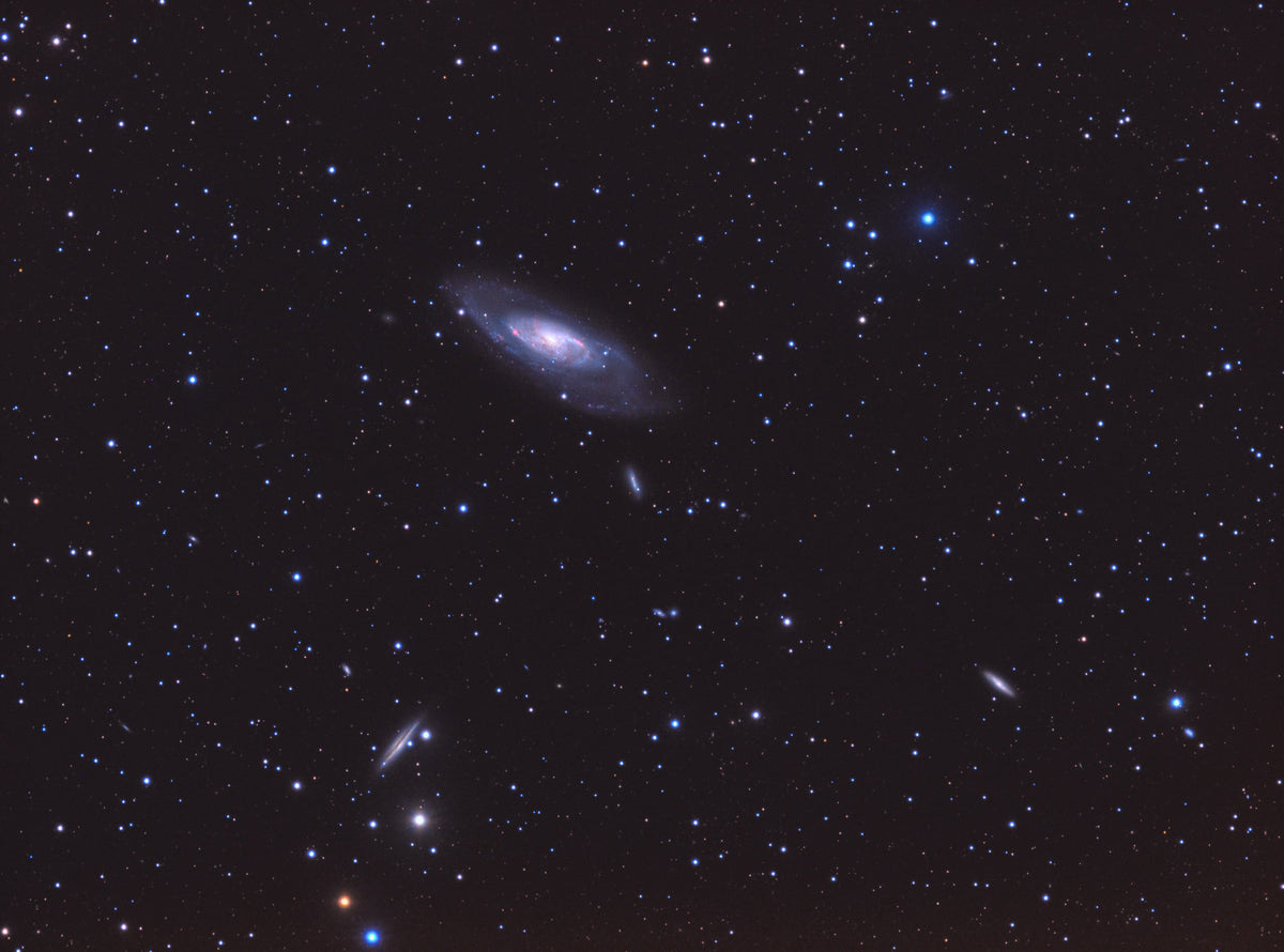 Galaxie Messier 106 en diagonale, avec un centre lumineux et un disque bleuté entouré d’étoiles.