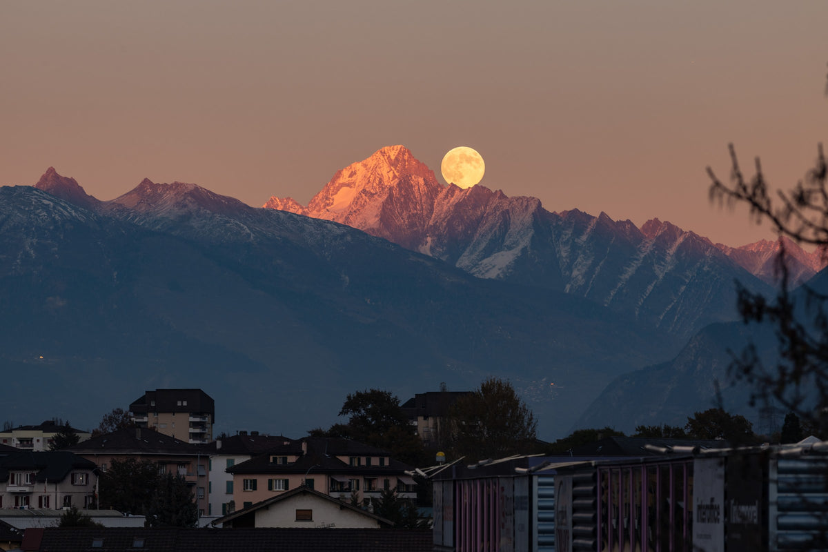 Lune orange près du sommet du Bietschhorn, au-dessus des montagnes enneigées et des bâtiments du premier plan.