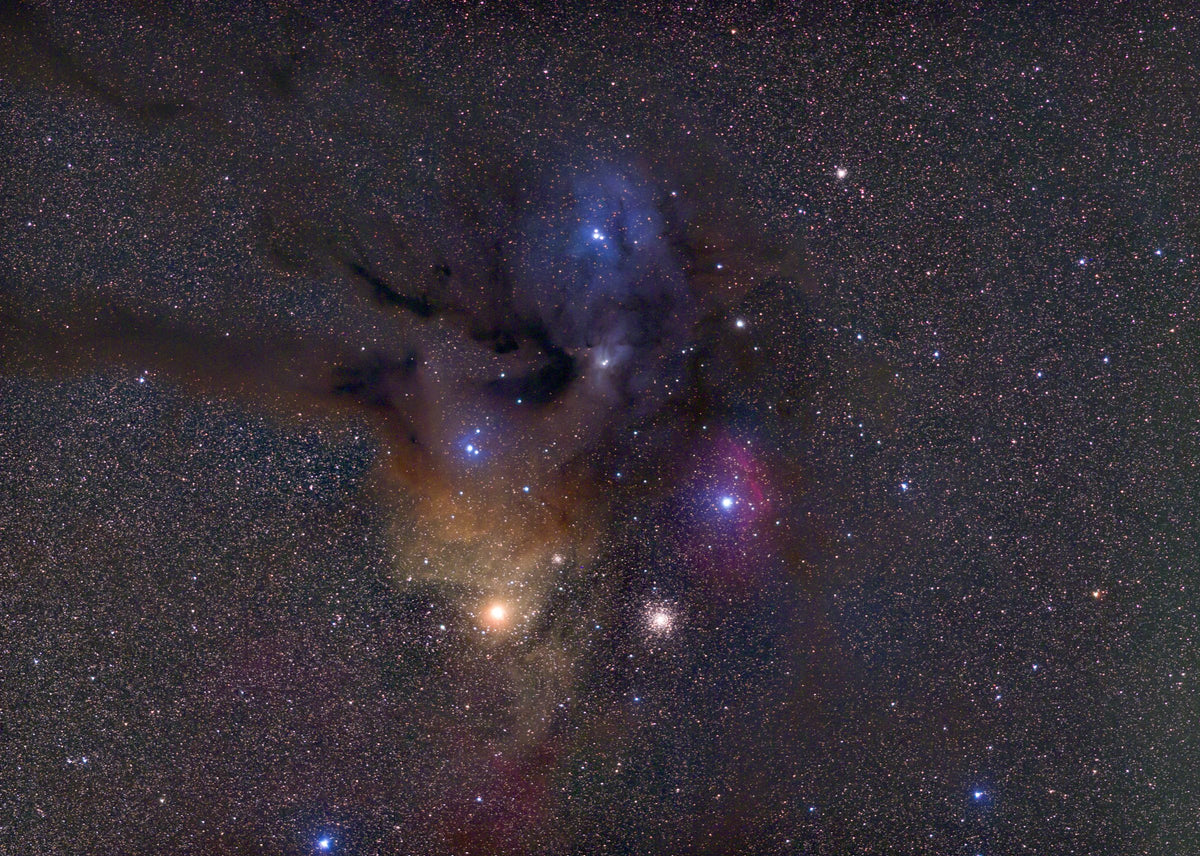 Nébuleuses bleues, roses et dorées autour d’étoiles brillantes, traversées par des filaments sombres de Rho Ophiuchi.