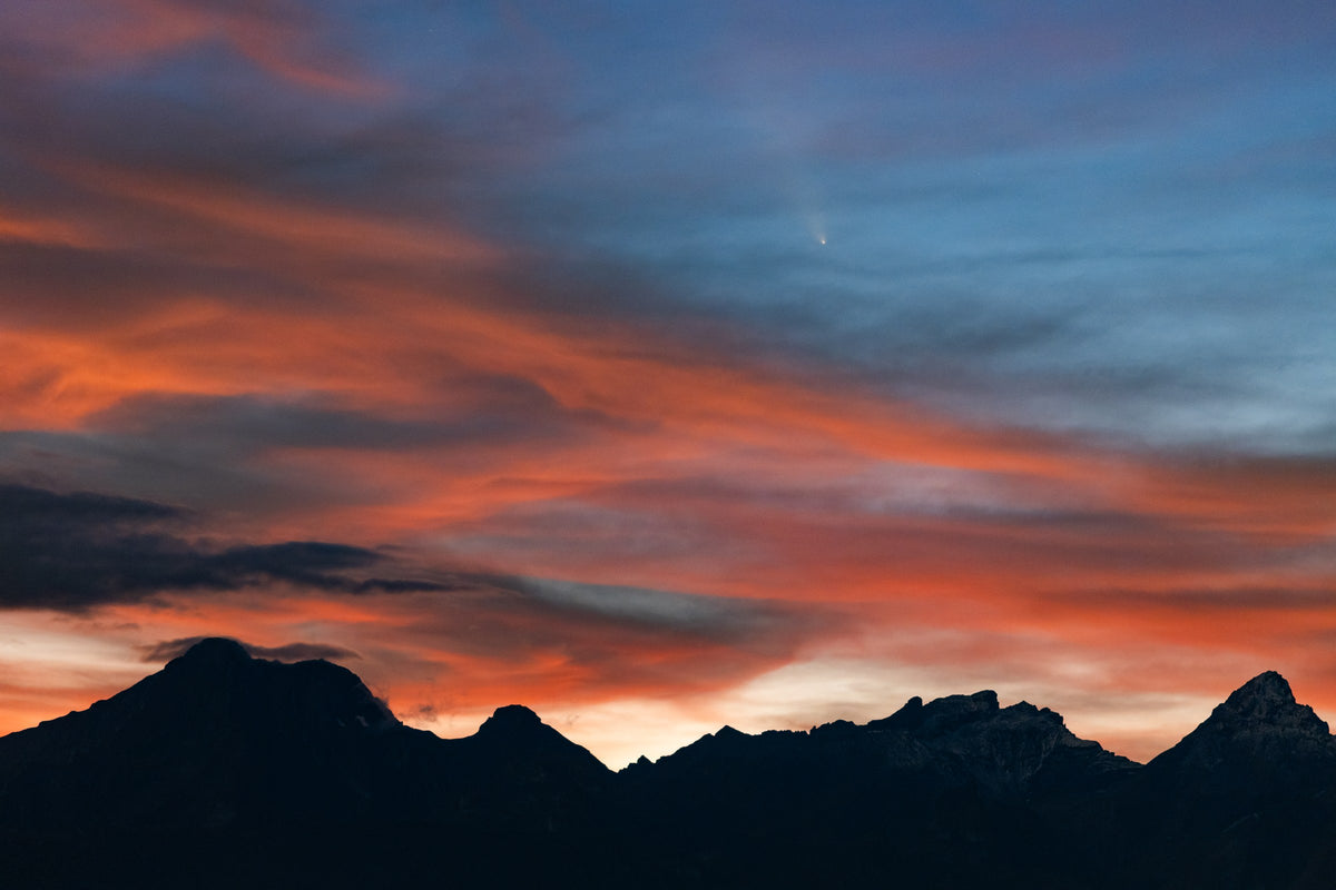 Ciel orange, rose et bleu au-dessus de montagnes sombres, avec la comète Tsuchinshan-ATLAS au crépuscule.