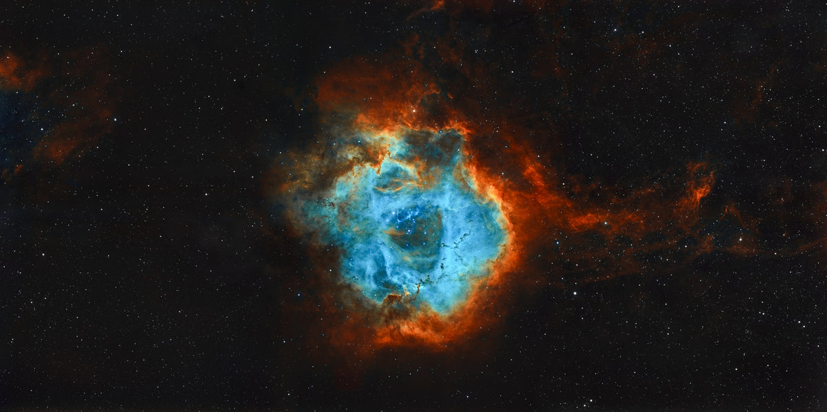 Nébuleuse de la Rosette aux contours orangés et au centre bleu, avec un groupe d’étoiles dans la cavité centrale.