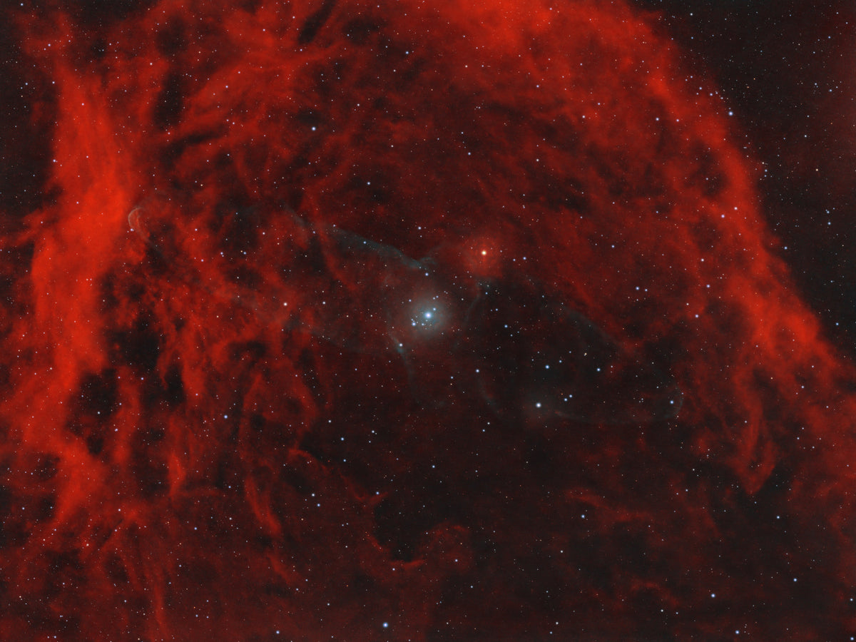 Vastes filaments rouges de Sh2-129 autour d’un champ d’étoiles, avec une très faible structure bleutée près du centre.