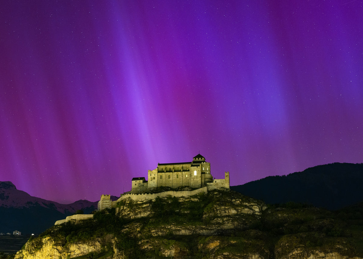 Colonnes violettes d’aurore boréale au-dessus de la basilique de Valère illuminée sur sa colline.
