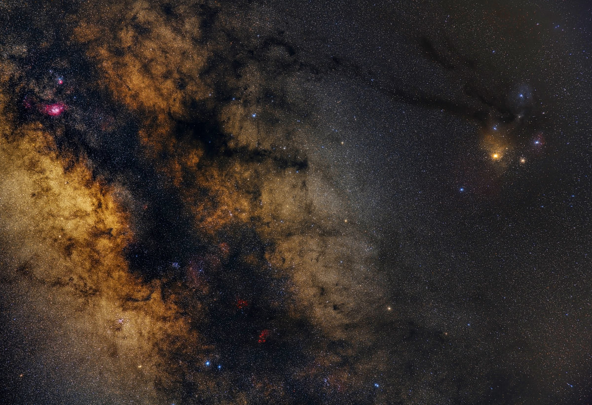 Nuages dorés et bandes noires de la Voie lactée à gauche, région colorée de Rho Ophiuchi autour d’une étoile orange à droite.