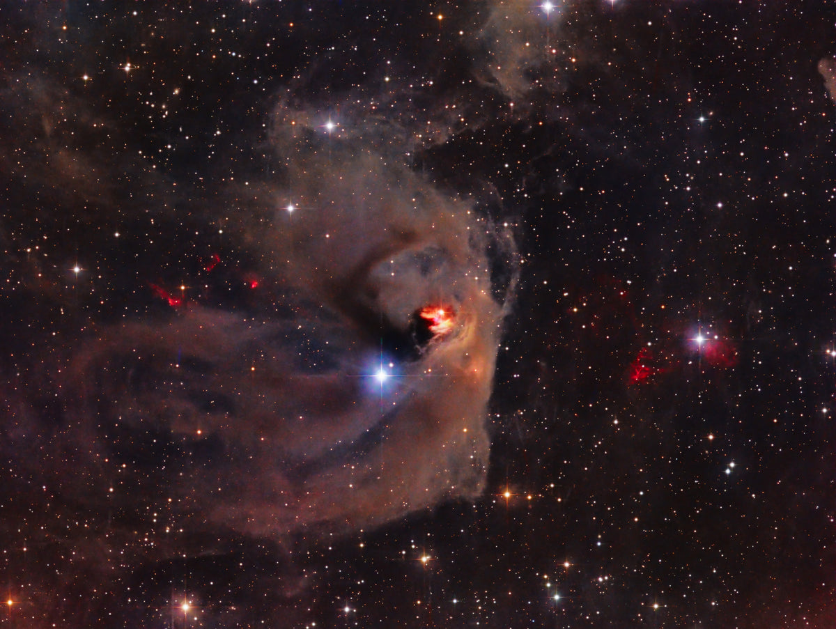Petites nébulosités bleutées et orangées dans des nuages bruns, entourées d’étoiles sur fond sombre.