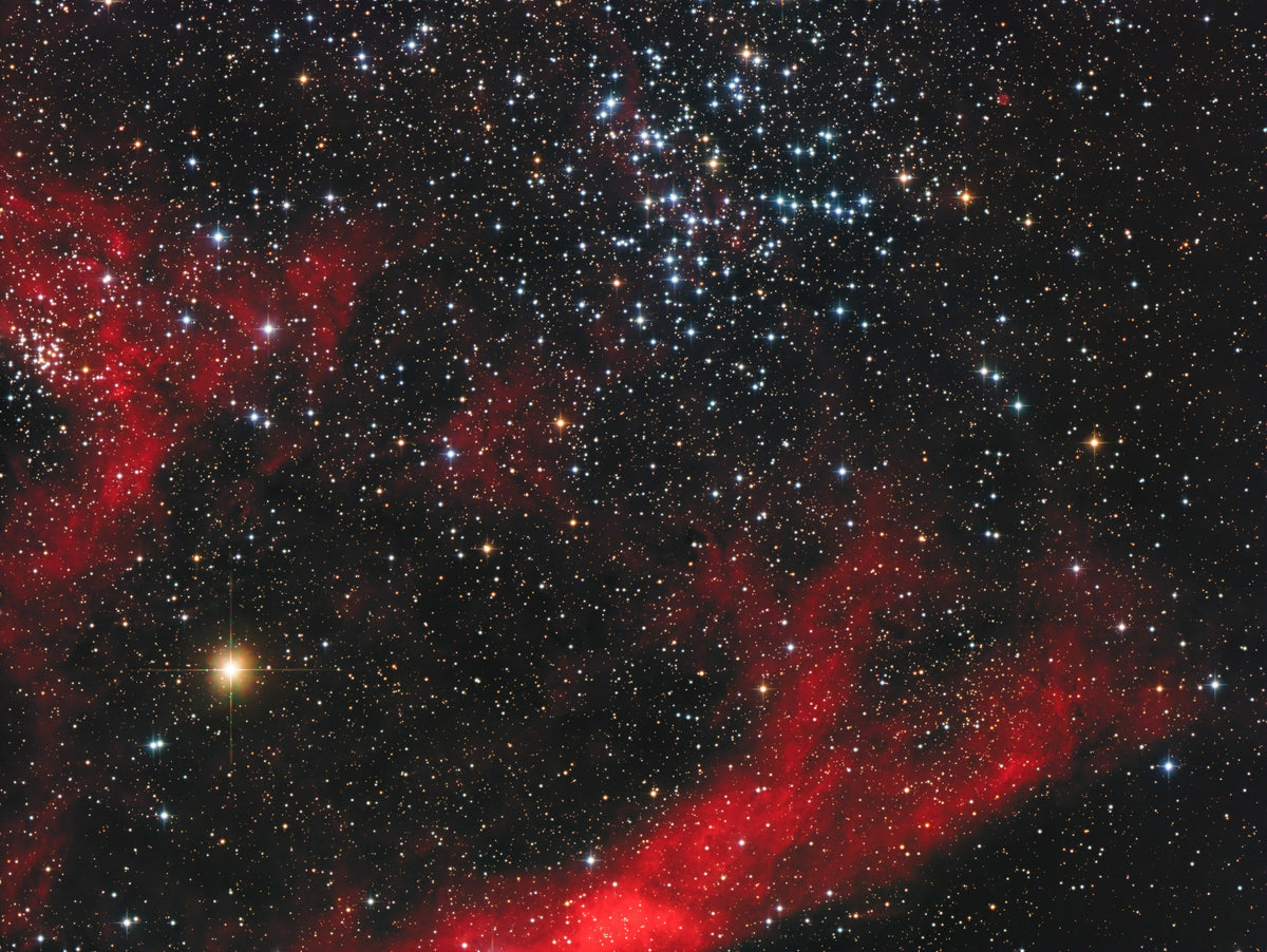Regroupement d’étoiles bleutées de Messier 38 au-dessus de grandes nébulosités rouges dans un champ dense.