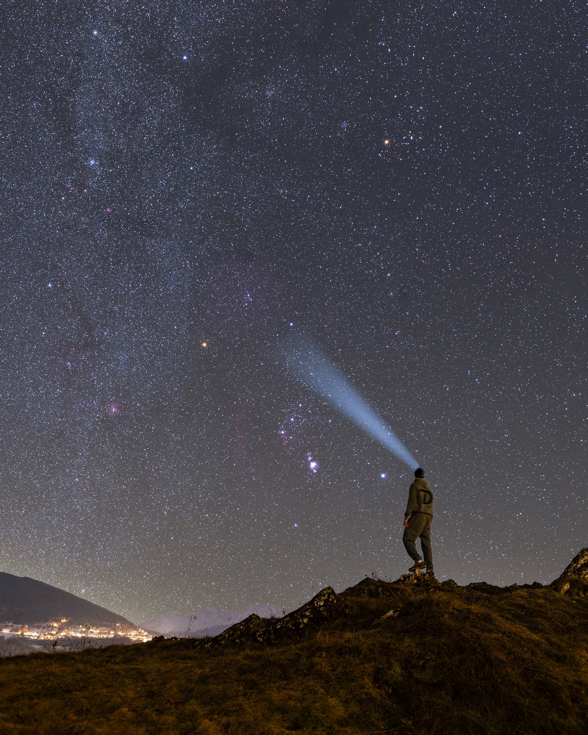 Personne en silhouette sur un relief rocheux, sous un ciel d’hiver étoilé et la région lumineuse d’Orion.