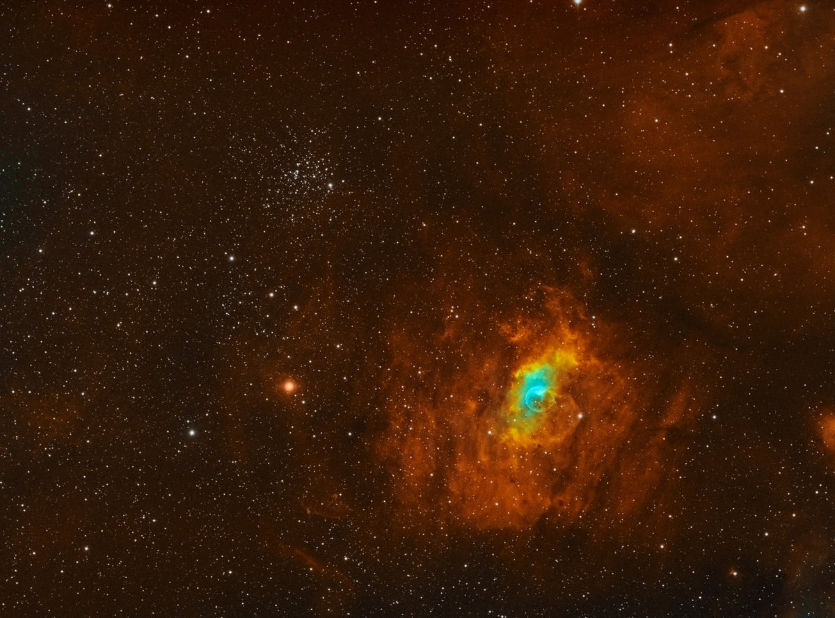 Petite bulle bleutée dans des nébulosités orangées, accompagnée d’un amas compact d’étoiles.