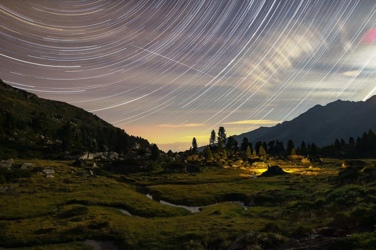 Traînées d’étoiles et nuages au-dessus d’un paysage de rochers, de végétation et de montagnes à Nendaz.
