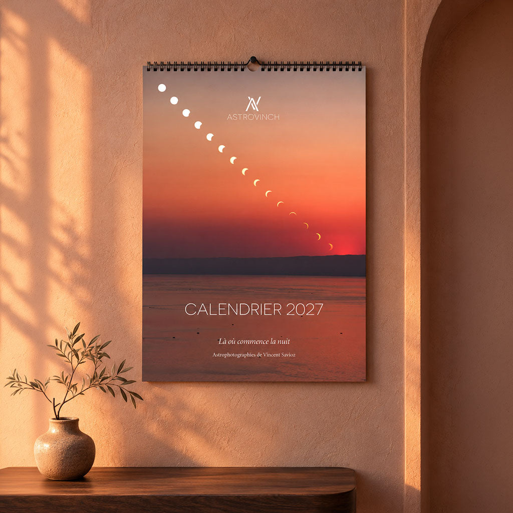 Calendrier AstroVinch 2027 suspendu à un mur, avec sa couverture et sa reliure spirale visibles.